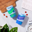 Two bottles from the Teens' Dream Team Starter Pack rest on a white surface near a plant, wooden board, towel, clock, and gummy vitamins—ideal for supporting teen multivitamin needs.