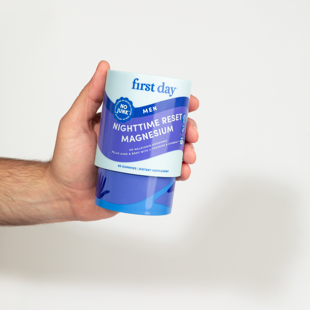 Hand holding a container of 'first day' magnesium supplement with a white background