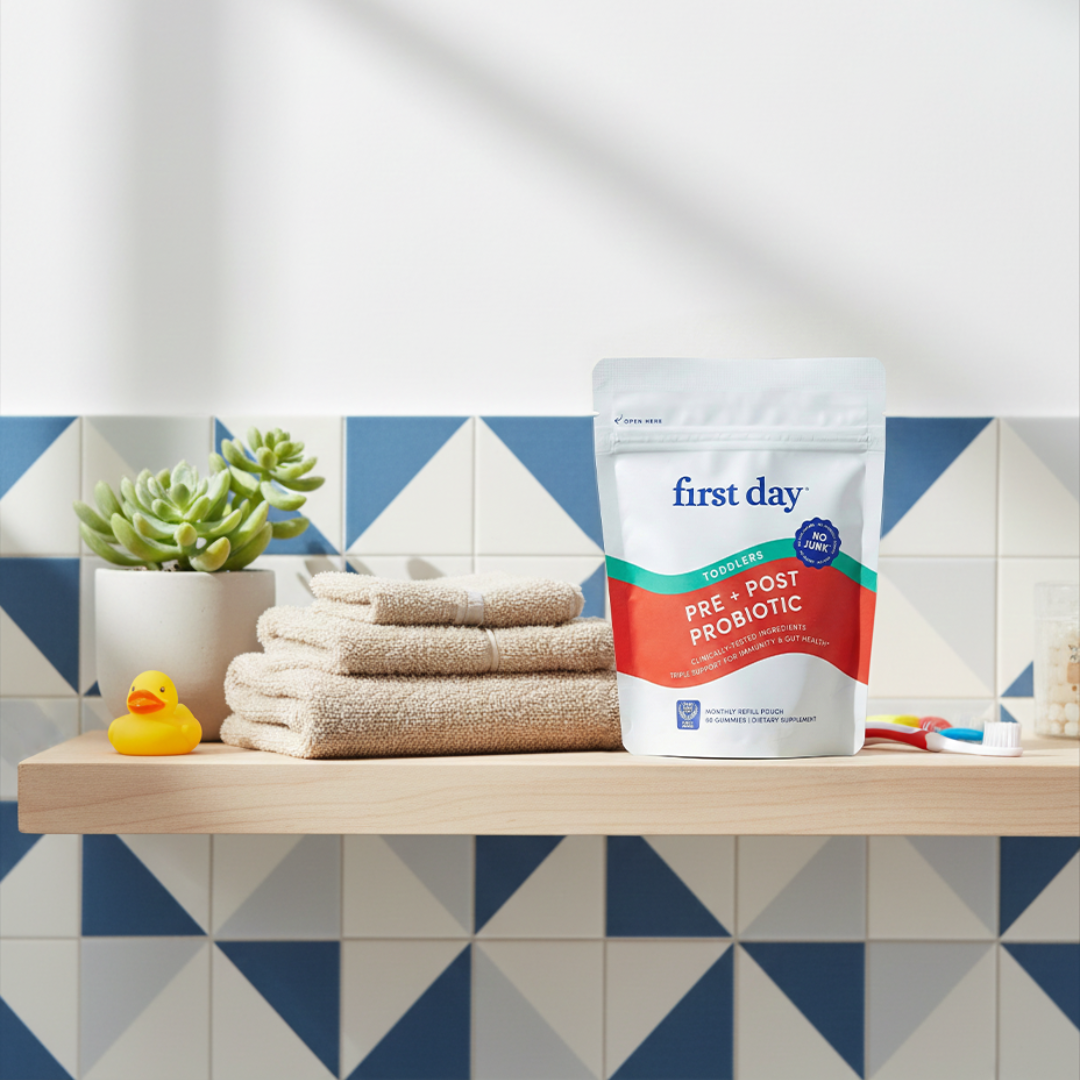 First Day pre+post probiotic package on a bathroom shelf with towels and a rubber duck.