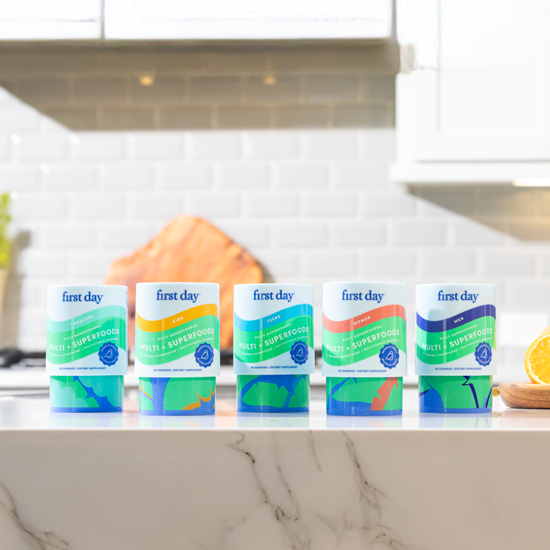 Multivitamin bottles on a kitchen counter with ingredients in the background