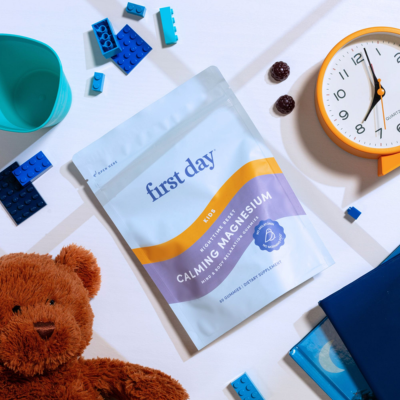 Package of 'first day' calming medication on a table with a teddy bear, clock, and building blocks.