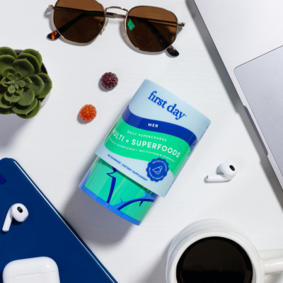 Container labeled 'first day' with sunglasses, plant, and electronic devices on a white surface