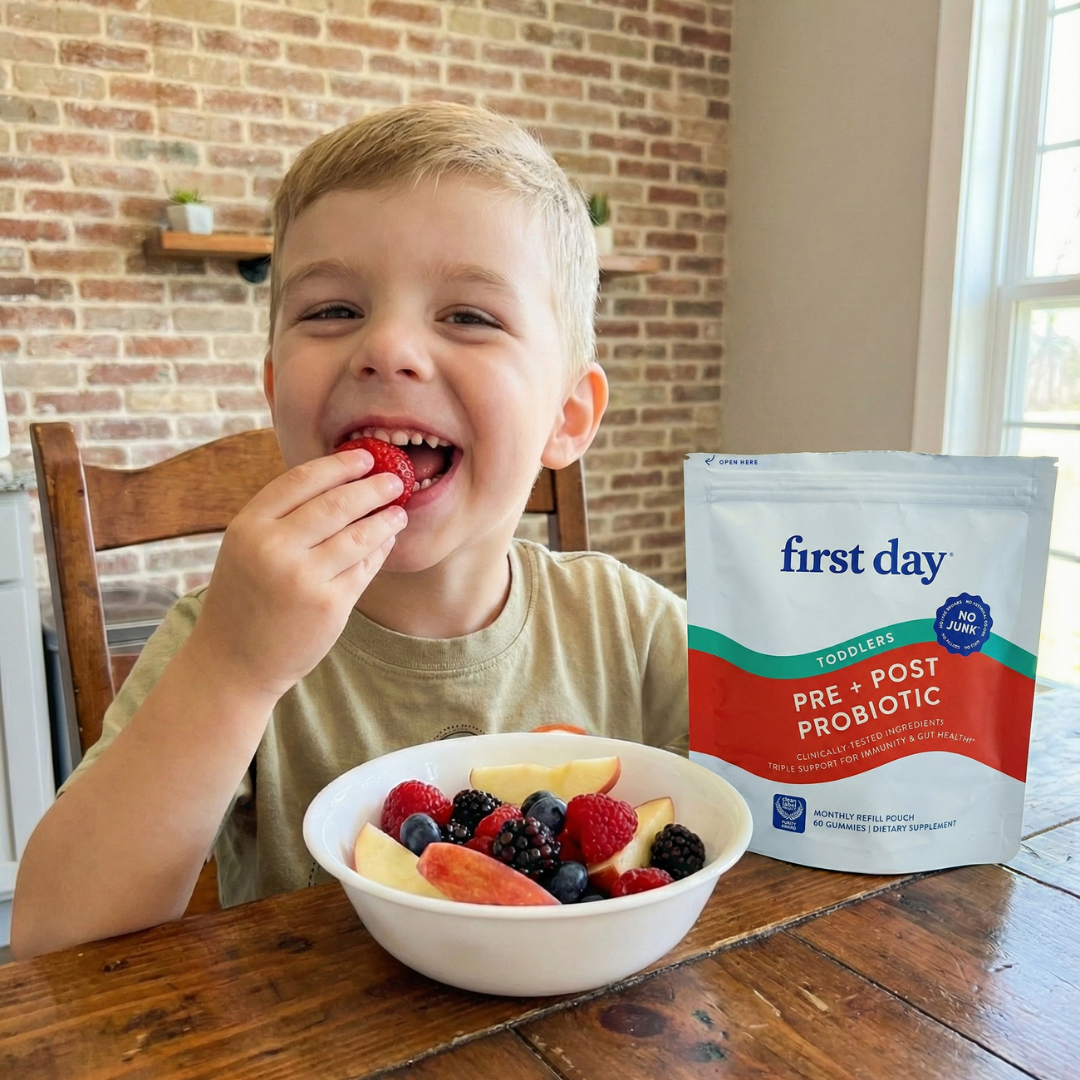 Child eating fruit with a bowl of berries and a 'first day' probiotic package on a wooden table.