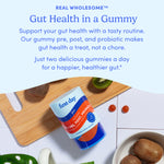 A container of Men's 3-in-1 Pre+ Post+ Probiotic gummies sits on a wooden board with sliced kiwi, cherry tomatoes, and a spoon. Text above highlights digestive wellness—just two gummies a day for a healthier gut.