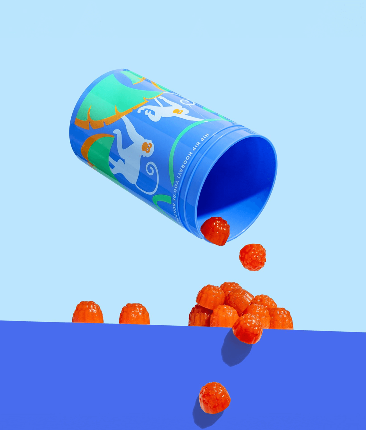 Blue cylindrical container with colorful design spilling orange gummy bears onto a blue surface.