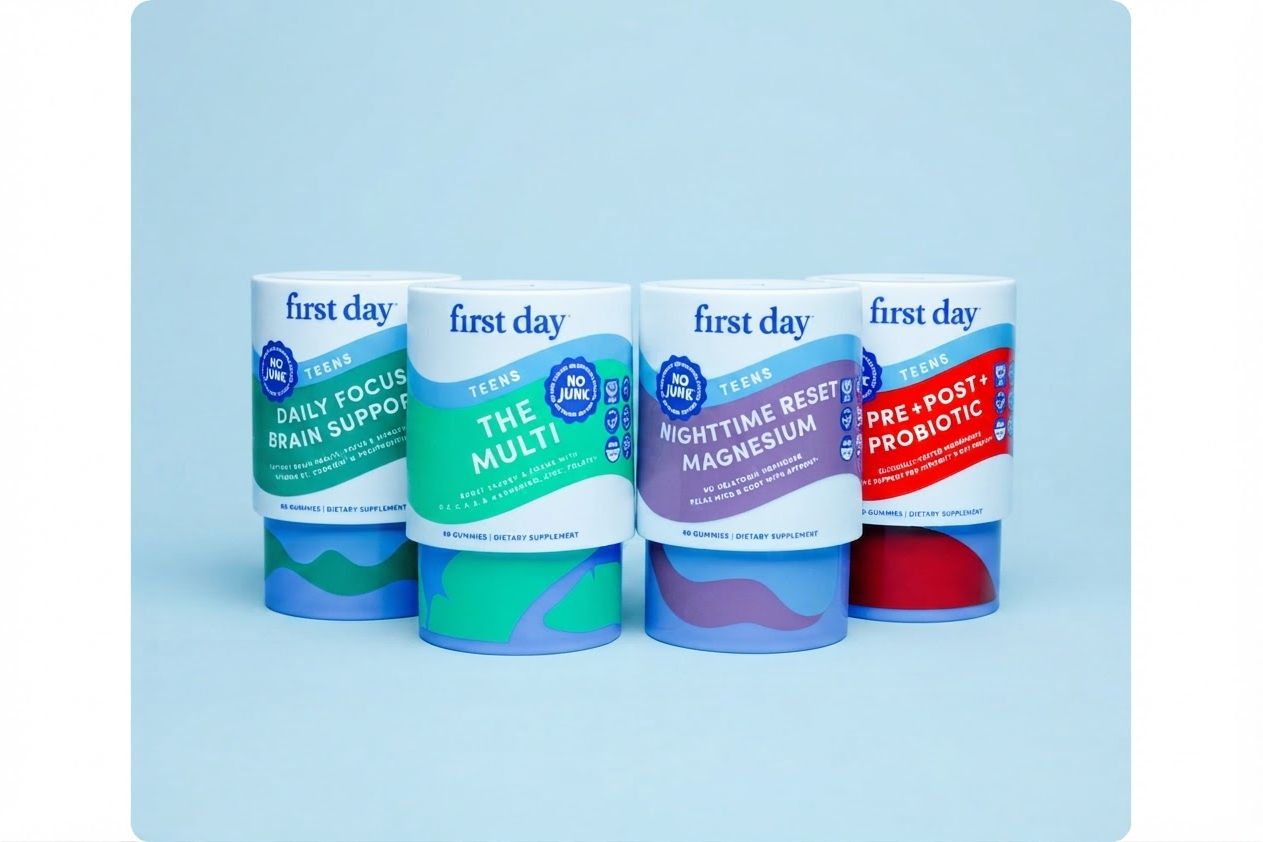 Four First Day supplement tubes arranged in a row on a light blue background. The tubes are white with colorful labels in green, teal, purple, and red, and feature the First Day brand name and product names: Daily Focus Brain Support, The Multi, Nighttime Reset Magnesium, and Pre-Post Probiotic.