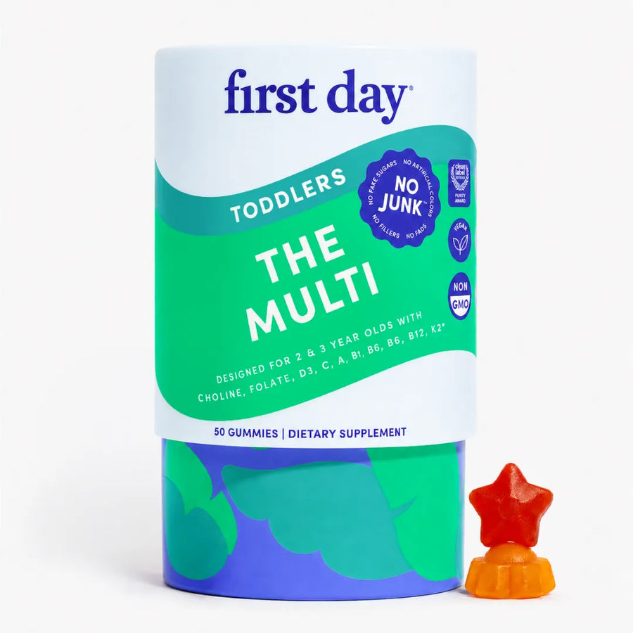 A cylindrical container of First Day The Multi dietary supplement gummies for toddlers, shown on a clean white background with a small red and orange star-shaped gummy candy placed in front of the container.